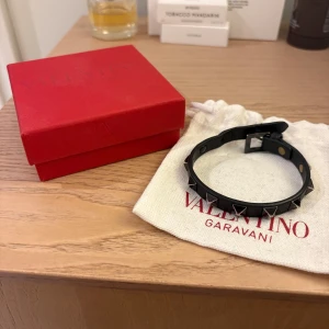 Valentino Garavani svart armband - Svart armband från Valentino Garavani i läder med ikoniska nitar i svart färg. Justerbart spänne för perfekt passform. Kommer med original ask och dustbag. Perfekt accessoar för sommaren. Kom DM för fler frågor🙌