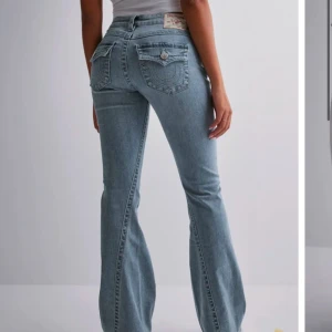 Ljusblå bootcut jeans från True Religion - Säljer ett par ljusblå jeans från True Religion med bootcut passform och snygga detaljerade bakfickor med lock och knapp. Har endast använt dem två gånger och använder inte längre så därför säljer jag