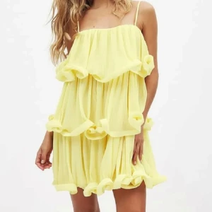 Gul volangklänning med tunna axelband  - Säljer en söt gul klänning med volanger och tunna axelband. Klänningen har en luftig och flowy passform, är kort och tillverkad i ett lätt, plisserat material. Perfekt för varma dagar och ger en riktigt somrig känsla. Slutsåld på NA-KDs hemsida. HELT NY med prislapp kvar. Säljer då jag beställde både 36 och 38, men 38 satt bäst. Testar att sälja innan jag returnerar till NA-KD då jag vet att klänningen är eftertraktad och populär💛💛 storlek 38. Orginalpris: 730