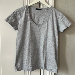 Grå t-shirt med v-ringning från Brandy Melville - Säljer denna T-shirt från Brandy Melville. Nästan helt oanvänd.