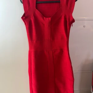 Röd bandageklänning by Lipsy London - Snygg röd bandageklänning från Lipsy London med markerad midja och breda axelband. Klänningen är figurnära och har en cool struktur i tyget. 