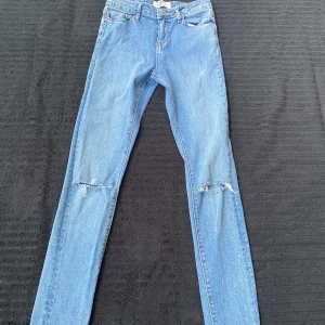 Blå skinny jeans med slitningar på knäna - Säljer ett par blå skinny jeans med slitna detaljer över båda knäna. Klassisk femficksmodell med normal passform i midjan och smala ben. Perfekta för en avslappnad och trendig look.