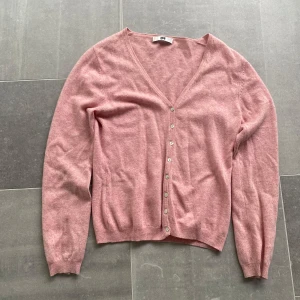 Rosa kofta med v-ringning  - Säljer en mjuk rosa kofta med v-ringning och knappar framtill. Tröjan har långa ärmar och ribbade muddar vid ärmslut och nederkant. Perfekt att slänga över en topp för en enkel och snygg look.