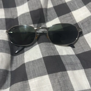 Svarta solglasögon från Ray-Ban - Snygga svarta solglasögon från Ray-Ban med smal metallbåge och mörka glas. Klassisk oval form som ger en stilren look. Perfekta för dig som vill ha en tidlös accessoar med ikonisk design.