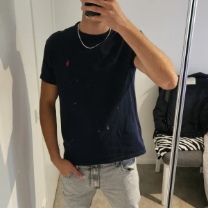 Mörkblå t-shirt från Polo Ralph Lauren - Snygg mörkblå t-shirt från Polo Ralph Lauren med klassisk passform. T-shirten har korta ärmar och är gjord i mjuk bomull. På bröstet finns den ikoniska röda broderade polospelaren. Perfekt basic med stilren vibe.
