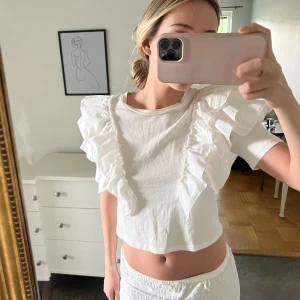 Vit t-shirt med volangdetaljer - Säljer en vit t-shirt med korta ärmar och stora volangdetaljer framtill. Perfekt för dig som vill ha en söt och trendig topp till sommaren. Enkel att matcha med både jeans och kjol🤍