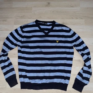 Randig tröja från Lyle & Scott - Säljer en blå och svart randig tröja från Lyle & Scott med v-ringning och broderad gul logga på bröstet. Tröjan har långa ärmar och är tillverkad i mjukt material, perfekt för en stilren och vintage vardagslook. Den originella storleken är XL men den sitter som en M. Skriv gärna vid minsta fråga, pris kan diskuteras.