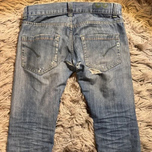 Dondup jeans med slitningar - Säljer ett par blå jeans från Dondup med slitningar och hål på både fram- och baksida. De sitter ganska slim upptill och lite lösare nedtill. Snygga slitningar där fram. Däremot är de lite småhål vid rumpan som man ser på andra bilden vilket inte syns när man har på sig de , därav lite lägre prisklass. Priset är ej hugget i sten. Bara att skriva vid minsta fundering!