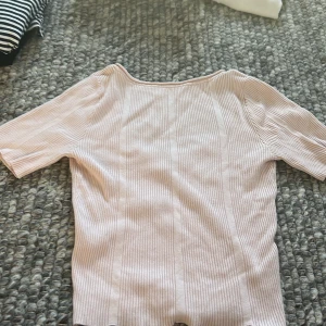 Ljusrosa ribbad topp med kort ärm - Säljer en ljusrosa ribbad topp med korta ärmar och djup rundad halsringning. Toppen är croppad och har en tight passform, perfekt för vår och sommar. Superenkel att matcha med jeans eller kjol!