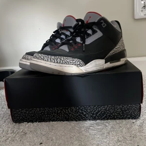 Nike Air Jordans Black Cement - Säljer ett par klassiska Nike Air Jordans Black Cement med svart skinn, grå och röda detaljer samt ikoniskt elefantmönster runt tån dom är bra skick knappt använda bara gulning vid sulan då de är den gamla realesen 
