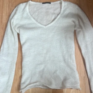 Vit v-ringad långärmad tröja från Brandy Melville - Säljer en enkel och stilren vit långärmad tröja med v-ringning. Perfekt att matcha med jeans eller kjol för en clean look. Mjuk och skön mot huden. Materialet är mohair liknande. oversized fit