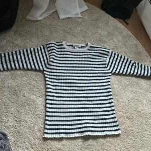 Randig ribbad tröja från Primark - Säljer en ribbad långärmad tröja från Primark i vitt och marinblått med klassiskt randigt mönster. Tröjan har rund halsringning och är perfekt för en avslappnad stil.