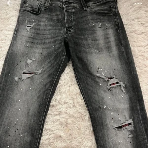Svarta slitna jeans med färgstänk - Säljer ett par svarta jeans från Jack & Jones som inte kommer inte användning. Knappt använda och köpte dem för 1000 nypris.