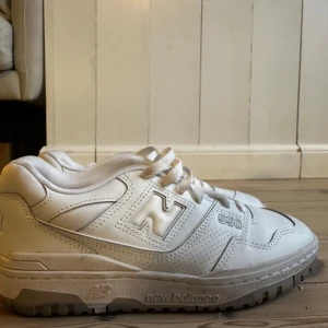 Vita New Balance 550 sneakers - Säljer ett par fräscha vita New Balance 550 sneakers med klassisk siluett och perforerade detaljer på sidorna. Skorna har snörning och en chunky sula som ger en sportig vibe. Perfekta för dig som gillar stilrena och bekväma sneakers.