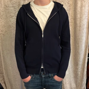 Kashmir/merino hoodie - Mörkblå hoodie från Livanno med dragkedja framtill och huva med snören. Jackan har två fickor och ribbade muddar vid ärmslut och nederkant. Perfekt för en avslappnad stil.