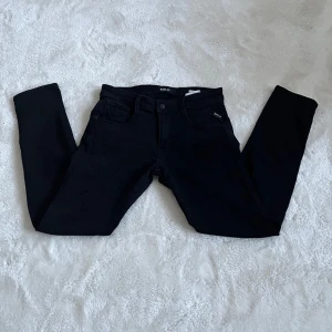 Svarta anbass jeans från Replay - Säljer ett par svarta anbass jeans från Replay med klassisk femficksdesign och raka ben. Byxorna har diskreta sömdetaljer på bakfickorna och en liten Replay-logga vid fickan. Perfekta för en stilren och avslappnad look. Funkar till det mesta!