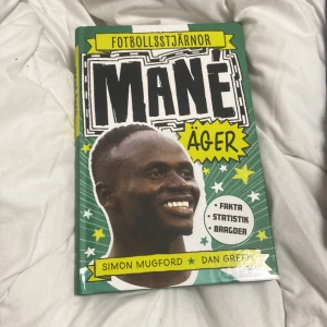 Fotbollsstjärnor: Mané äger - En inspirerande bok om fotbollsstjärnan Sadio Mané, skriven av Simon Mugford och Dan Green. Boken har ett grönt och gult omslag med en stor bild på Mané och innehåller fakta, statistik och bragder om hans karriär.