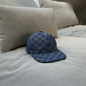 Blå keps från Gucci med GG-mönster - Snygg blå keps från Gucci med klassiskt GG-mönster över hela kepsen. Justerbart spänne baktill i blått läder och detaljer i metall. Perfekt accessoar för att lyfta din stil.