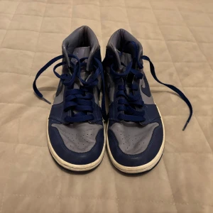Nike Air Jordan 1 Mid Iron Purple/Deep Royal Blue - Säljer ett par Nike Air Jordan 1 Mid  i färgerna iron purple och deep royal blue. Skorna har högt skaft, snörning och är tillverkade i skinn med blå och grå detaljer. Skriv för fler frågor eller bilder i chatten tack!