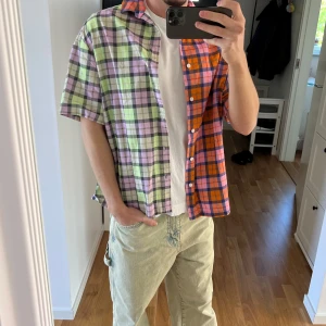 Färgglad rutig skjorta med kort ärm - Säljer en unik skjorta med kort ärm och rutigt mönster i orange, rosa, lila och grönt. Perfekt för dig som vill sticka ut med färg och mönster. Den är även tunn vilket är perfekt till sommaren.