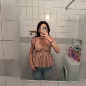 Rosa beige volangtopp med knytning från Lager 157 - Säljer rosa beige topp från Lager 157 med volangdetaljer på axlarna och knytning framtill. Toppen har v-ringning och är tillverkad i ett ribbat, lätt material. 🩷