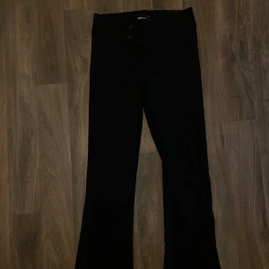 Lågmidjsde Svarta bootcut-byxor från Gina - Svarta byxor från Gina Tricot med bootcut-passform och låg midja. Byxorna har bred linning med två knappar framtill och är tillverkade i ett mjukt, stretchigt material. Perfekta för en trendig och bekväm look. Använda 1 gång. De är cirka 102 cm från midjan ner. 🌸