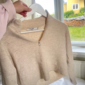 Beige croppad stickad tröja med dragkedja från NA-KD - Säljer en beige croppad stickad tröja från NA-KD med halv dragkedja framtill och hög krage. 