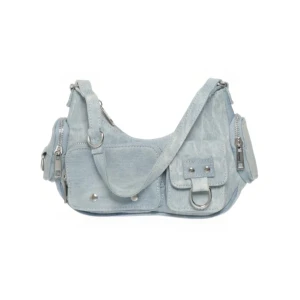 Ljusblå axelväska i jeans - Trendig ljusblå axelväska i jeansmaterial med flera fickor och silvriga metalldetaljer. Väskan har justerbar axelrem och dragkedjor samt dekorativa ringar framtill. 