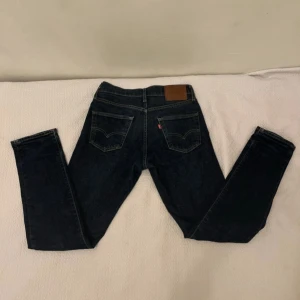 Mörkblå Levis jeans 511 - Säljer ett par mörkblå Levis jeans med klassisk femficksdesign och raka ben. Jeansen har bruna sömmar, läderpatch bak och Levis röda etikett på bakfickan. Perfekta för dig som gillar tidlös denimstil. W 29 L 32