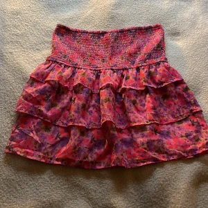 Blommig volangkjol från Bik Bok - Supersöt kort blommig kjol från Bik Bok i rosa och lila toner. Kjolen har smock i midjan och dubbla volanger.