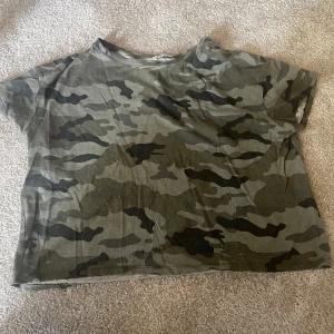 Camouflage t-shirt - Säljer en kortärmad t-shirt med klassiskt camouflage-mönster i gröna och svarta toner. Perfekt för en avslappnad och cool stil. T-shirten har en rak passform och rund hals.