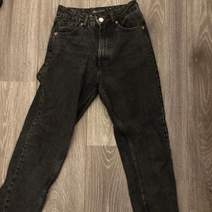 Svarta jeansbyxor från Zara - Säljer ett par svarta jeansbyxor (mom jeans)  från Zara med klassisk femficksdesign och raka ben. Byxorna har hög midja och stängs med knapp och dragkedja. Perfekta till många olika outfits och enkla att matcha.