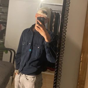 Mörkblå skjorta från Christian Dior - Säljer en mörkblå  overshirt/skjorta från Christian Dior med klassisk krage och snygga metallknappar med logga. Skjortan har två bröstfickor och är långärmad. Perfekt för dig som vill ha en stilren och exklusiv look. Ny pris var         12 000kr men sänker den till 7000kr