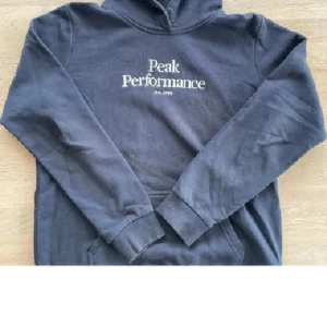 Mörkblå hoodie från Peak Performance - Säljer en mörkblå hoodie från Peak Performance med vit logotyp på bröstet. Tröjan har långa ärmar, huva och en klassisk känguruficka framtill. Perfekt för en avslappnad stil. I storlek Medium är prutbar vid snabbaffär skriv om du har några frågor eller funderingar 