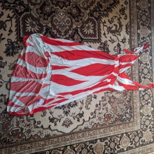 Rödvit långklänning med mönster - Säljer en långklänning med rödvita vågiga mönster och halterneck. Klänningen har en luftig passform och knyts i nacken. Perfekt för sommardagar eller när du vill sticka ut med färg och mönster.