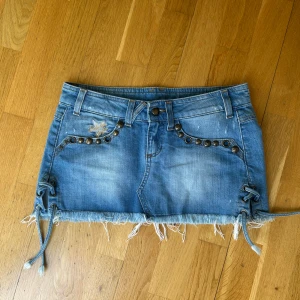 Blå jeanskjol med nitar och snörning - Säljer en jättesnygg blå jeanskjol med slitna detaljer, nitar vid fickorna och snörning i sidorna.