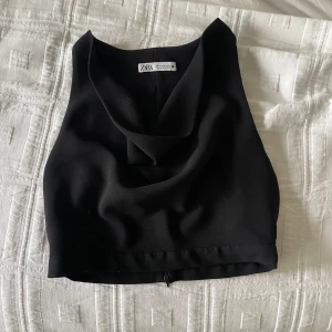 Svart kostym topp från Zara - Säljer en svart croppad linnetopp från Zara med snygg draperad urringning. Toppen är ärmlös och har en stilren, minimalistisk design som passar perfekt till många olika outfits.