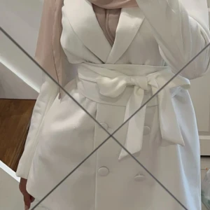 Kavaj - Snygg vit kavaj/kavajklänning med knytbälte i midjan. Perfekt för studenten eller andra eleganta tillfällen. Använd endast en gång. Köpt från bohoo. Storlek 34 🤍 