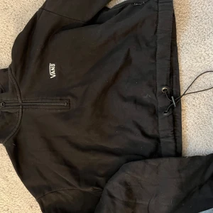 Svart tröja från Vans med halv dragkedja - Svart tröja från Vans i storlek XS med halv dragkedja framtill och justerbar dragsko nedtill. Tröjan har en enkel och stilren design med Vans-logga på bröstet. Perfekt för en avslappnad streetstil.