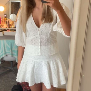 Vit kortklänning med broderade detaljer - Superfint vitt kort set med v-ringning och broderade hål. Klänningen har puffiga trekvartsärmar och markerad midja med volang i kjolen. Perfekt för sommarens tillfällen! Man kan ha på sig blusen och kjolen separat, så om någon vill köpa en av klädesplaggen är det bara att höra av sig! Men ser helst att någon köper hela settet. Settet är slutsålt på h&m och använt en gång! 