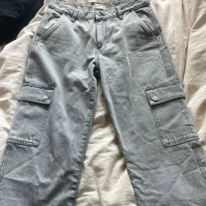 Grå cargo jeans - Fina raka grå cargo jeans med fina ditaljer, såsom fickor på benen och snörning vid byxslutet.