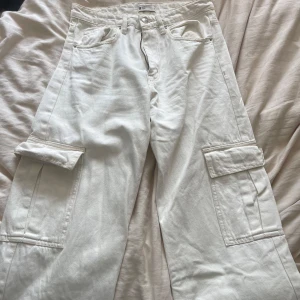 Vita cargopants från Gina Tricot - Säljer ett par vita cargopants från Gina Tricot med raka ben och stora fickor på sidorna. Byxorna har normal passform och är tillverkade i bomull. Perfekta för en avslappnad och trendig stil.