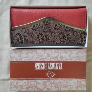 Röd plånbok med paisleymönster och hjärtspegel - Säljer en snygg röd plånbok från Fantasy Design med paisleymönster och silverdetaljer. Insidan har ett hjärtformat spegel och flera fack för kort. Perfekt accessoar för dig som vill sticka ut lite extra!