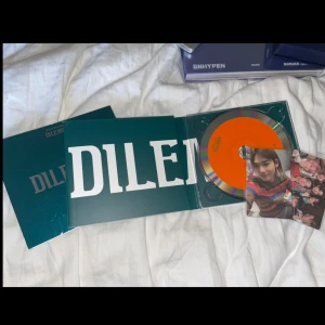 ENHYPEN DILEMMA album - Säljer ENHYPENs album 'DILEMMA' med grön omslag, orange CD och tillhörande photocard. Albumet innehåller fotobok och exklusiva bilder på medlemmarna. Perfekt för samlare av K-pop och ENHYPEN-fans.
