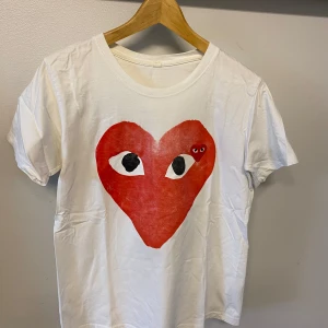 Vit t-shirt från Comme des Garçons Play - Vit t-shirt med stort rött hjärta och ögon-tryck på bröstet, samt ett mindre hjärta med ögon inuti det stora. Klassisk och stilren design som sticker ut.
