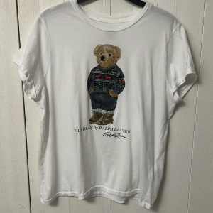 Vit t-shirt med björntryck från Ralph Lauren - Vit t-shirt från Ralph Lauren med ikoniskt Polo Bear-tryck framtill. Klassisk rund hals och storlek S.