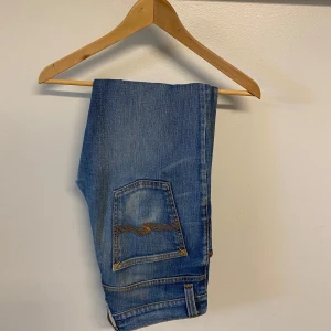 Blå jeansbyxor från Nudie Jeans - Säljer ett par klassiska blå jeans från Nudie Jeans med tydliga gula sömmar och ikonisk bakficka. Perfekta för dig som gillar en tidlös stil och vill ha ett par jeans som funkar till det mesta. Skriv om du har några frågor😁