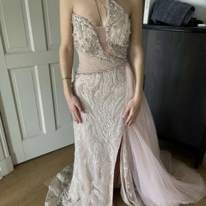 Ljus rosa  långklänning med paljetter och slits - Säljer en elegant champagnefärgad långklänning med glittriga paljetter, öppen rygg och en axelbandslös design. Klänningen har en vacker slits framtill och ett långt släp i tyll. Perfekt för bal eller fest. Den är endast använd en gång och är som helt ny. Nypris ligger på 9000kr 