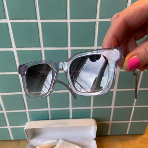 Lila solglasögon från CHIMI x H&M - Snygga solglasögon i transparent lila från CHIMI x H&M. Rektangulär form med bred båge och mörka glas. Kommer med vit hård förvaringsask och putsduk. Perfekt accessoar för att lyfta din stil.