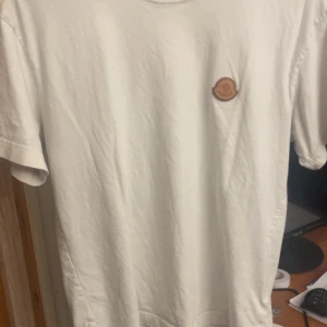 Vit t-shirt från Moncler med logga - Säljer en stilren vit t-shirt från Moncler med klassisk rund hals och liten Moncler-logga på bröstet. Perfekt för dig som gillar enkla och exklusiva plagg. T-shirten är i mjuk bomull och har korta ärmar. Såklart äkta, ny pris 3200kr mitt 1000kr priset är ej hugget i en sten